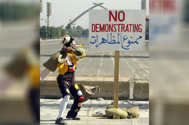 Bağdat'ta palyaço kıyafeti giymiş Iraklı bir adam Protestolar yasak yazılı direğe vuruyor, 6 Kasım 2003.jpg