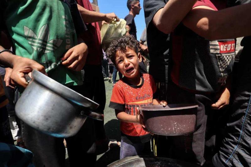 Gazze Şeridi'nin merkezindeki Nuseyrat mülteci kampında bir yiyecek dağıtım noktasındaki Filistinliler sıcak yemek almak için toplanırken bir çocuk ağlıyor / Fotoğraf: AFP
