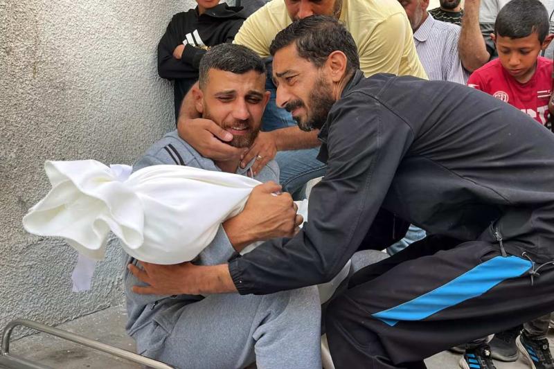 Gazze'de İsrail bombardımanında hayatını kaybeden bir kişinin cansız bedenine sarılan iki adam