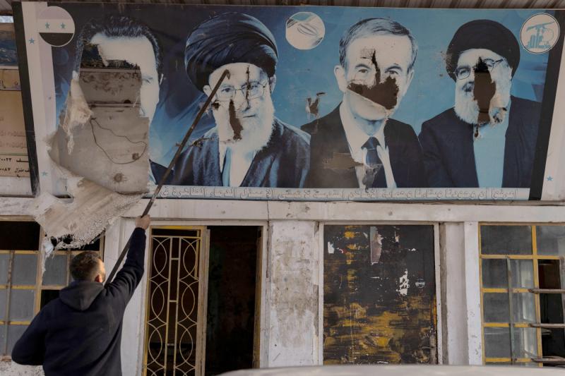 Bir işçi, Halep kırsalındaki Nubl'da bir benzin istasyonundaki Beşşar Esed, Hafız Esed, Hasan Nasrallah ve Ali Hamaney'in posterlerini yırtıyor 11 Aralık 2024 / Fotoğraf: Reuters