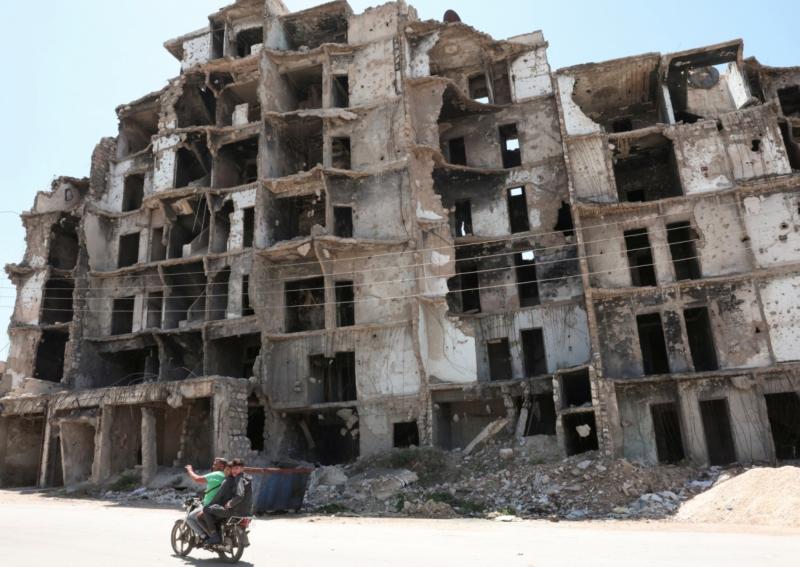 Halep’te hasar görmüş bir binanın önünden motosikletle geçenler, 14 Mayıs 2025 / Fotoğraf: Reuters