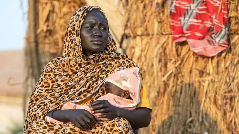 Yerinden edilmiş bir anne olan Malka, şiddetli akut yetersiz beslenmeden muzdarip bir yaşındaki kızı Sahar’ı, Gedaref Eyaleti’ndeki Elhoury yerinden edilmiş kişiler toplanma noktasındaki evinin dışında taşıyor / Fotoğraf: Ahmed Mohamdeen Elfatih- UNICEF Yerinden edilmiş bir anne olan Malka, şiddetli akut yetersiz beslenmeden muzdarip bir yaşındaki kızı Sahar’ı, Gedaref Eyaleti’ndeki Elhoury yerinden edilmiş kişiler toplanma noktasındaki evinin dışında taşıyor / Fotoğraf: Ahmed Mohamdeen Elfatih- UNICEF