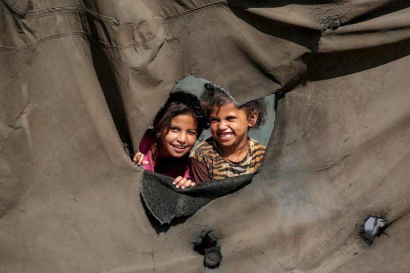 Çocuklar, Gazze Şeridi'nin merkezindeki Nuseyrat'ın kuzeyinde yerinden edilmiş kişiler için kurulan bir kampta, çadırdaki delikten bakıyorlar, 7 Ekim 2025 / Fotoğraf: AFP