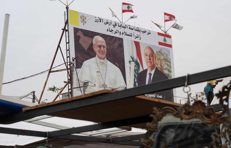 Beyrut'ta Papa XIV. Leo ve Lübnan Cumhurbaşkanı Joseph Avn'ın resimlerinin bulunduğu bir reklam panosunun yakınındaki ikinci el pazarında dolaşan insanlar, 29 Kasım 2025 / Fotoğraf: AFP