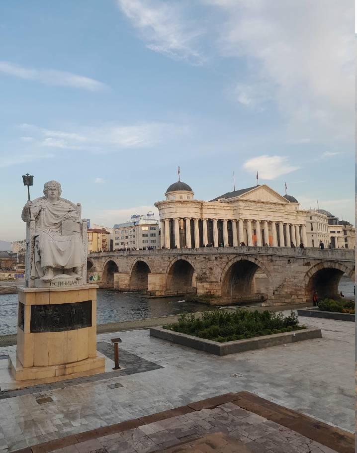 Solda I. Justinianus (namı diğer Büyük Justinianus) heykeli. Vardar Nehri, Kuzey Makedonya Arkeoloji Müzesi ve 15. yüzyılda Osmanlılar tarafından inşa edilen ünlü Taş Köprü