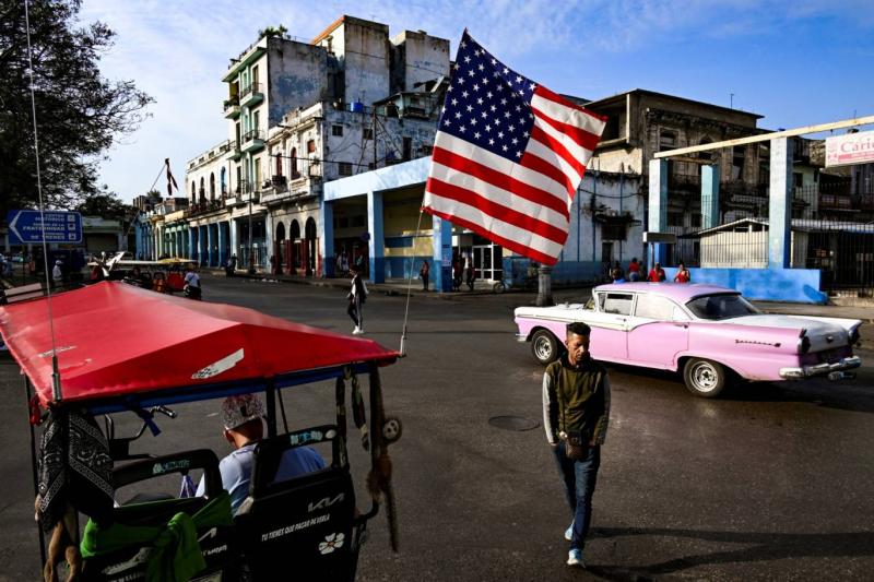 Havana'da Amerikan bayrağı taşıyan üç tekerlekli bisikletin yanında yürüyen bir adam / Fotoğraf: AFP
