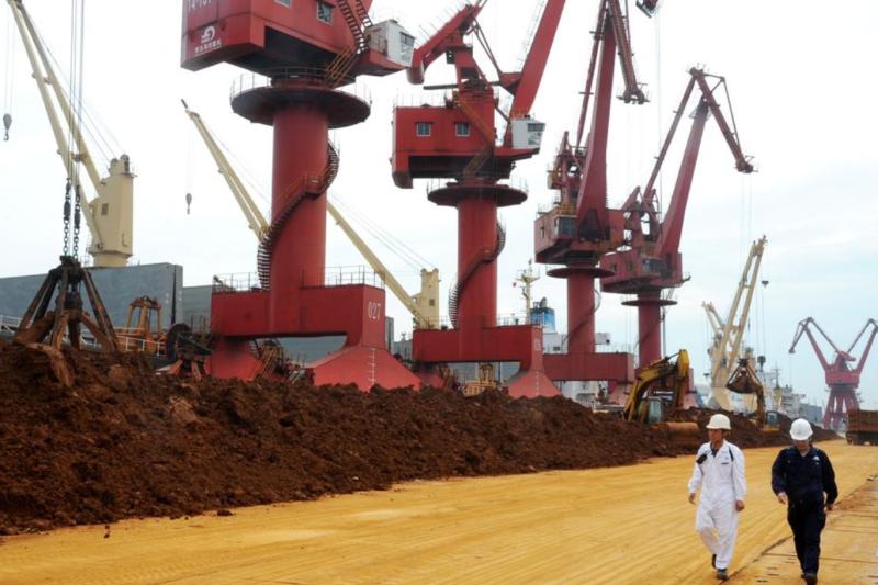 Çinli denetçiler, 22 Mayıs 2016’da Çin’in doğusundaki Jiangsu eyaletine bağlı Lianyungang Limanı’nda nadir toprak elementleri yığınlarının önünden geçiyor / Fotoğraf:  Wang Chun-AFP