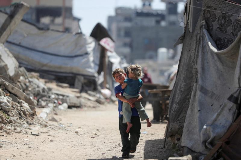 Gazze şehrinde, yıkılmış evlerin enkazları arasında, kucağında bir kız çocuğu taşıyarak yürüyen Filistinli bir çocuk, 11 Mayıs 2026 / Fotoğraf: Davud Ebu el-Kas-Reuters