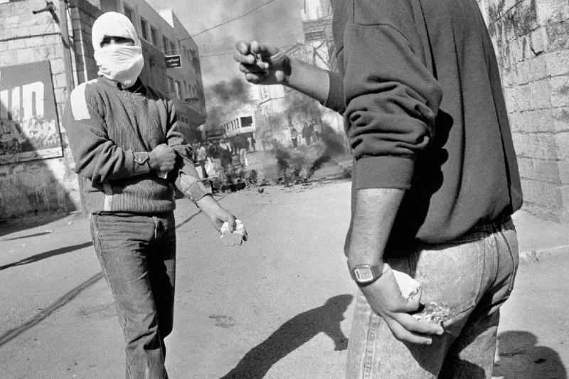 Batı Şeria, 1980'lerin sonu: Birinci İntifada sırasında barikatların ateşe verildiği sokak çatışmalarında, ellerinde taşlarla bekleyen yüzü maskeli Filistinliler