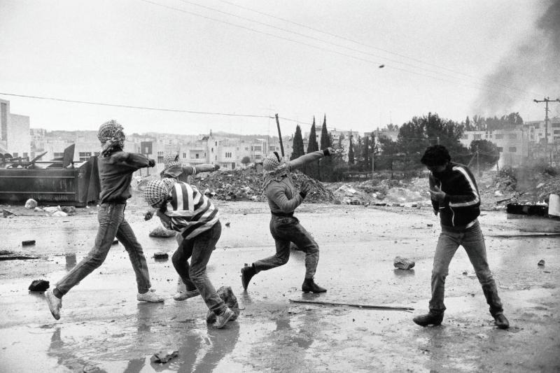 Birinci İntifada sırasında başlarına kefiye sarmış bir grup Filistinli genç, işgal altındaki topraklarda İsrail askeri güçlerine karşı taş fırlatırken (1988)