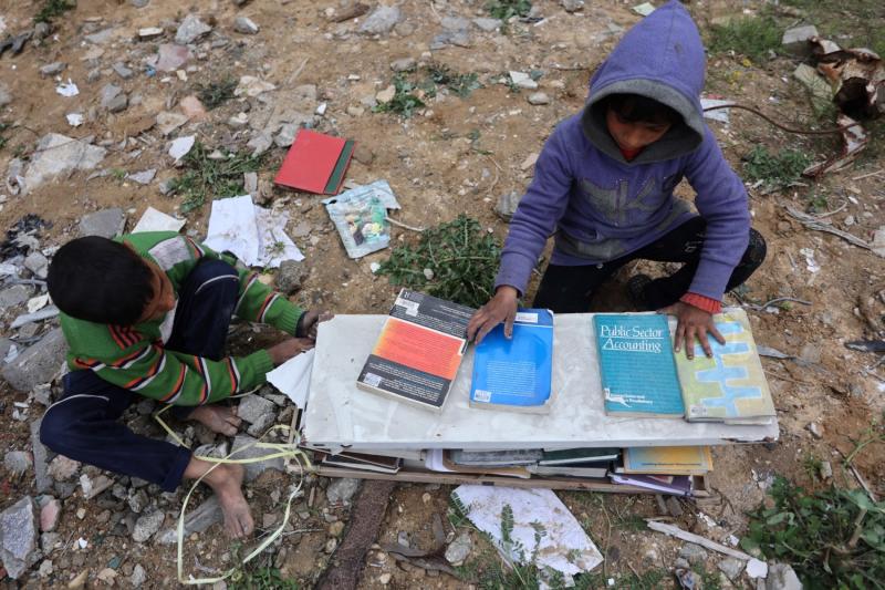 Filistinli mülteciler, yemek pişirmek için yakıt olarak kullanmak üzere Gazze’deki İslam Üniversitesi’nin enkazından kitapları topluyor, 21 Mart 2025 / Fotoğraf: Omar al-Qattaa-AFP