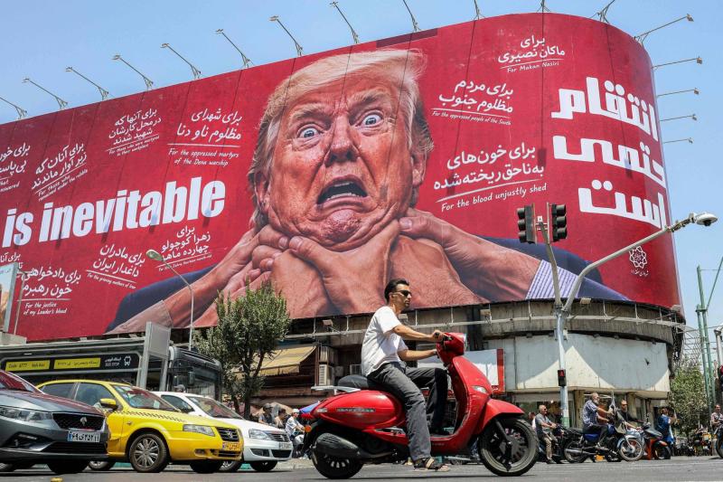 Tahran’da bir caddede, ABD Başkanı Donald Trump’ın resminin yer aldığı ve ‘İntikam kaçınılmaz’ yazan bir panonun önünden geçen yayalar, 28 Temmuz 2026 / Fotoğraf: AFP